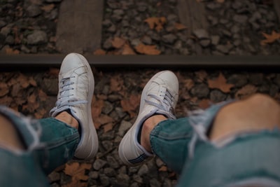 坐在铁路前面的人，穿着破旧的蓝色牛仔裤和白色低帮运动鞋